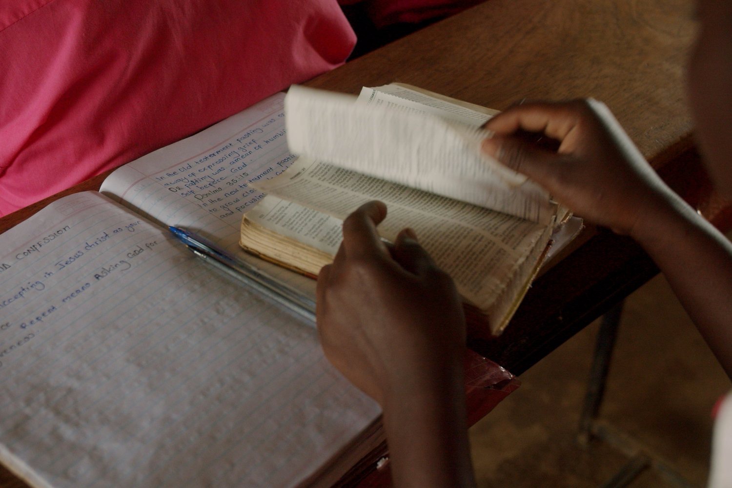 Hands turning the pages of a well-worn Bible beside handwritten study notes
